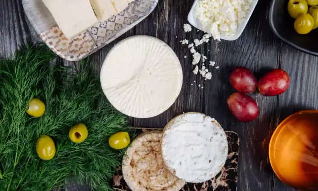 Różne rodzaje sera, oliwki, winogrona i koperek na ciemnym drewnianym tle.