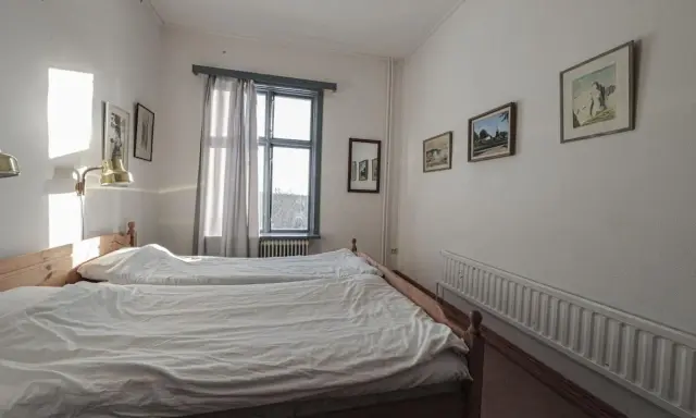 Två enkla sängar med vita täcken i ett rum på ett vandrarhem i Hjo. Solen lyser in genom fönstret.