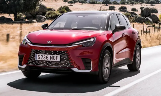El Lexus LBX rojo brillante se desplaza por una carretera rural, con un paisaje seco y rocoso de fondo.