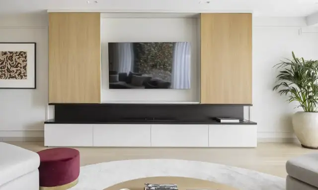 Un moderno mueble de salón con una gran televisión para poner la tele en medio del salón. Destacan los paneles de madera clara y los cajones blancos.