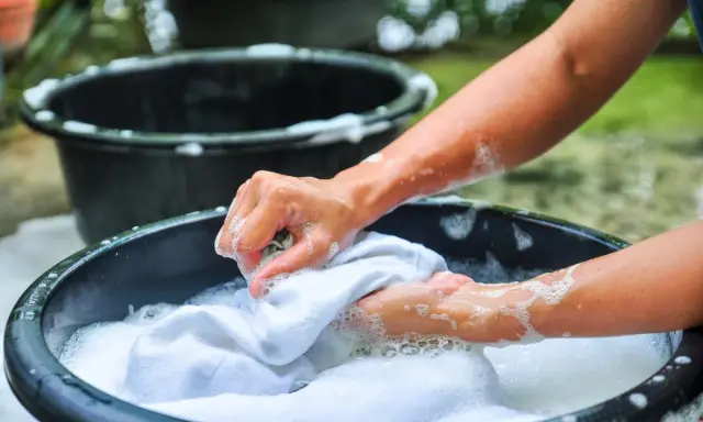 Manos lavando ropa blanca a mano en una tina con espuma, un método tradicional que explica qué significa lavado a mano en lavadora.