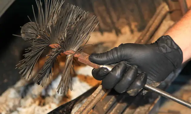 Main d'un ramoneur tenant une brosse pour cheminée. Le ramonage est essentiel pour l'assurance.