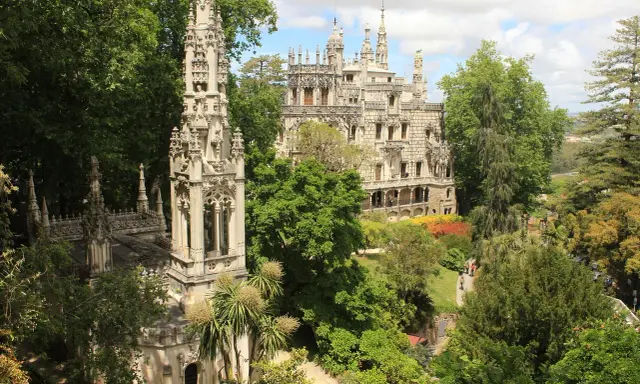 Sintra co zobaczyć: Quinta da Regaleira z wieżą i pałacem, otoczona bujną zielenią i kolorowymi rabatami.