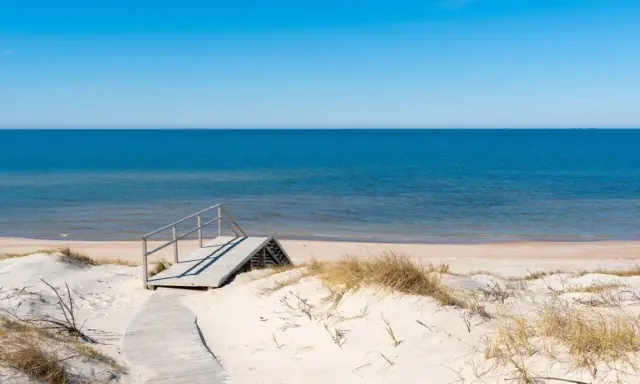 Drewniane schody prowadzące na piaszczystą plażę nad spokojnym Bałtykiem.