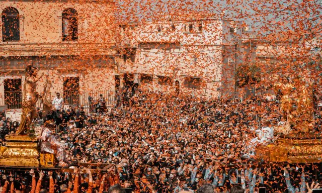 Folla festante sotto una pioggia di coriandoli arancioni, mentre si celebra cosa si festeggia a Pasqua con una processione solenne.