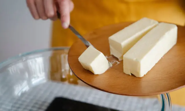 Ein Stück Butter wird mit einem Messer von einem Holzbrett gehoben, bereit für die Zubereitung von Butterschmalz.