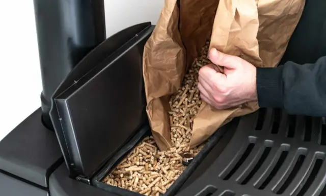 Persona rellena el depósito de una estufa de pellets con combustible.