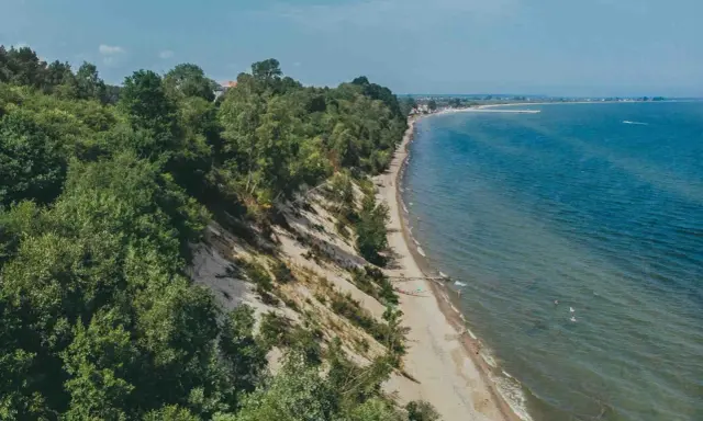 Malownicza plaża Mechelinki z zielonymi klifami i turkusowym morzem. Kilka osób odpoczywa na piasku, inni kąpią się w wodzie.
