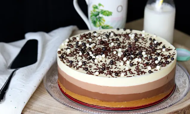 Deliciosa tarta de tres chocolates, con capas de blanco, con leche y negro, cubierta de virutas y bolitas de chocolate.