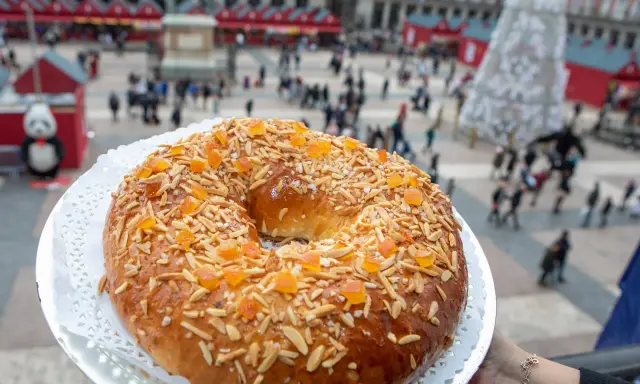 El mejor roscón de Madrid, adornado con almendras y fruta confitada, se presenta en la Plaza Mayor, un festín visual y delicioso.
