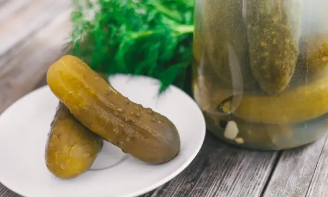 Dwa ogórki kiszone na talerzyku, obok słoik pełen kiszonków. Zastanawiasz się, dlaczego ogórki kiszone są puste w środku? To proces fermentacji!