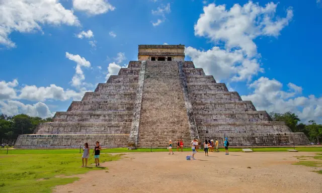 Majestatyczna piramida w Chichen Itza, z turystami podziwiającymi jej piękno na tle błękitnego nieba.