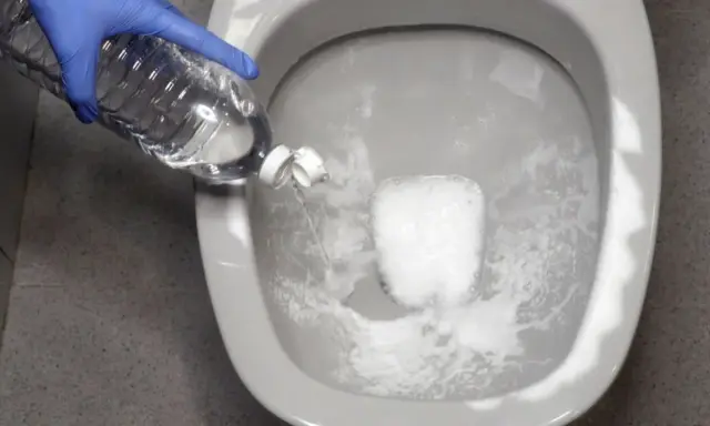 Guante azul vierte líquido de una botella en el inodoro. Solución para saber qué hacer si se atasca el vater.
