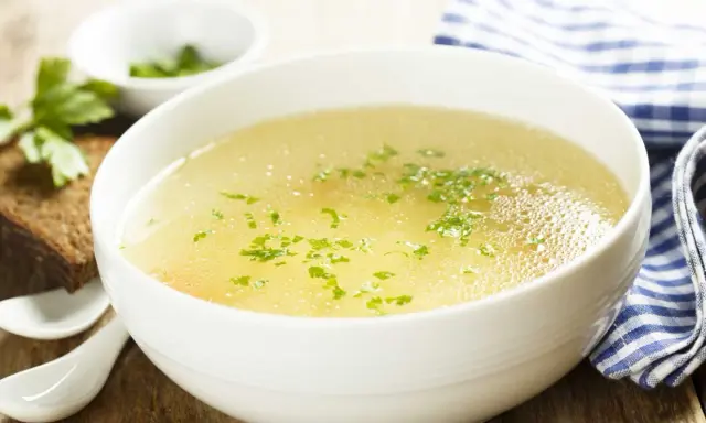 Aromaticzny rosół z perliczki, ozdobiony natką pietruszki, podany z kromką chleba. Idealny na chłodne dni.