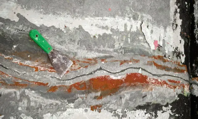 Espátula verde sobre pared agrietada con restos de pintura, como si se estuviera retirando el grout.