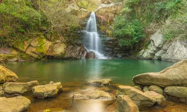 Cascada en un entorno verde con aguas cristalinas, evocando la belleza de las piscinas naturales de Cádiz.
