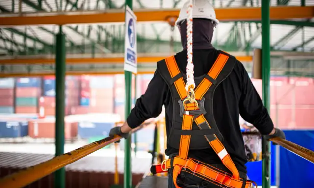 Trabajador con arnés de seguridad naranja y blanco, listo para trabajar en altura. La vida útil de un arnés de seguridad depende de su uso y mantenimiento.
