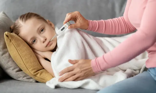Dziecko leży pod kocem, mama mierzy mu temperaturę. Wysoka gorączka u dziecka bez innych objawów martwi.