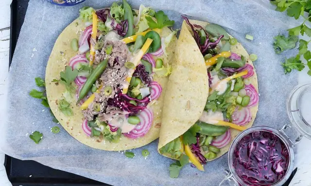 Två läckra tonfisk wraps fyllda med grönsaker, rödlök och en krämig sås. En burk med rödkålssallad står bredvid.