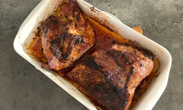 Två saftiga bitar av grillad pluma ligger i en vit ugnsform, redo att serveras.