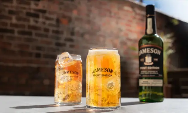 Dwa orzeźwiające drinki z lodem i butelka Jameson Stout Edition na tle ceglanej ściany.