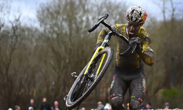 Wout van Aert kämpft sich im Schlamm durch ein hartes Cyclocross-Rennen, sein Körper und Rad sind komplett mit Dreck bedeckt.