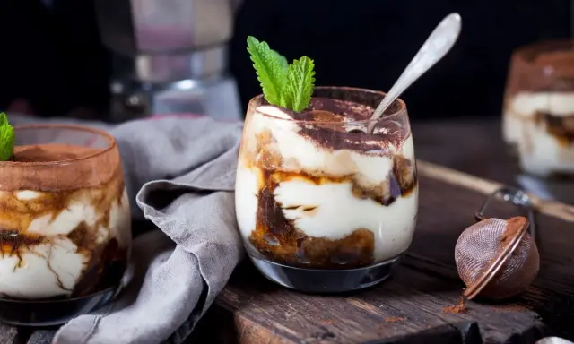 Pyszne tiramisu w pucharkach, udekorowane listkiem mięty, na drewnianej desce.