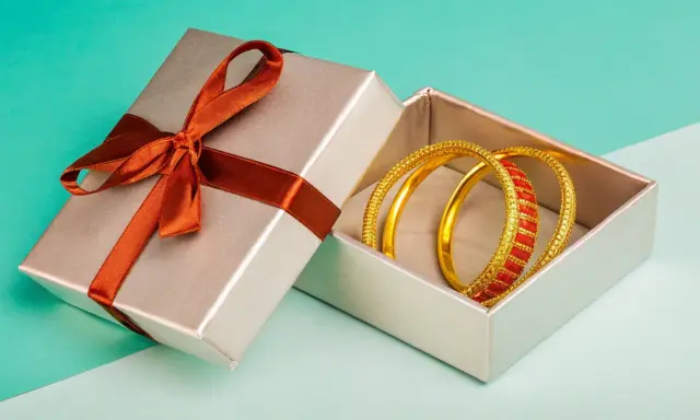 Scatola regalo aperta con bracciali dorati e rossi. Come capire se un bracciale è oro? Osserva la lucentezza e i dettagli.
