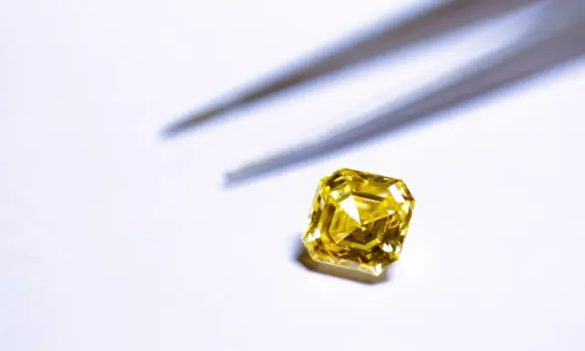 Un brillante giallo intenso, simile a un tesoro di **oro 18 carati**, attende di essere incastonato. Pinzette sfocate sullo sfondo.