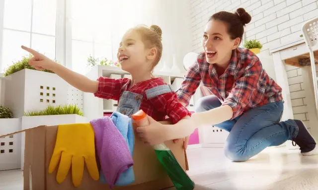 Mama i dziecko bawią się w sprzątanie, ucząc się jak nauczyć dziecko sprzątać. W kartonie są rękawice i płyn.