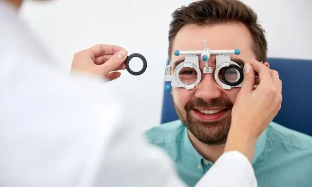 Mężczyzna uśmiecha się podczas badania wzroku w domu. Optometrysta wymienia soczewki w oprawce próbnej.