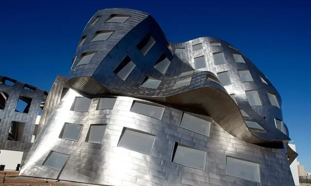 Edificio dalle forme ondulate e metalliche, una delle opere di Frank Gehry, con finestre quadrate e rettangolari.
