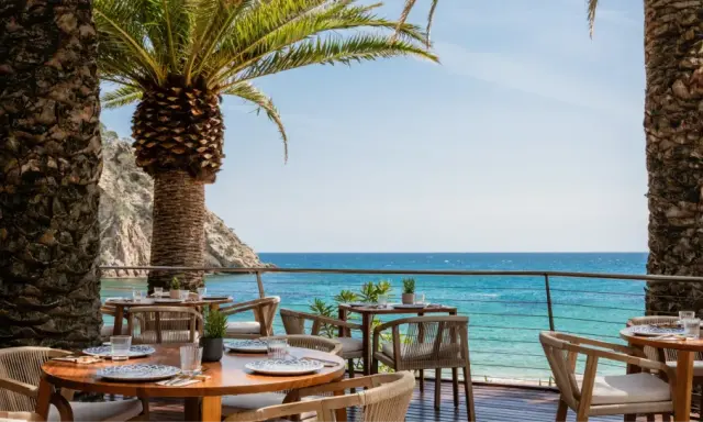 Mesas de restaurante con vistas al mar en el pola giverola resort, bajo palmeras.