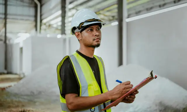 Un ingeniero de estructuras con casco y chaleco reflectante anota datos en una libreta, supervisando la construcción.