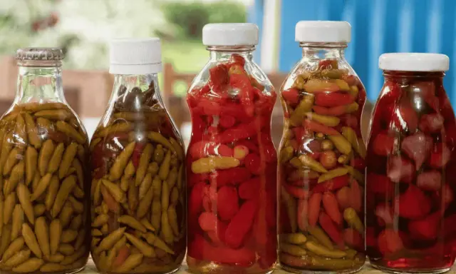 Bouteilles de piments verts et rouges marinés, prêts pour une recette de pickles maison.
