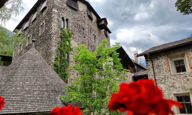 Il castello di Campo Tures, con le sue mura in pietra e il tetto a scandole, si erge maestoso tra il verde e fiori rossi.