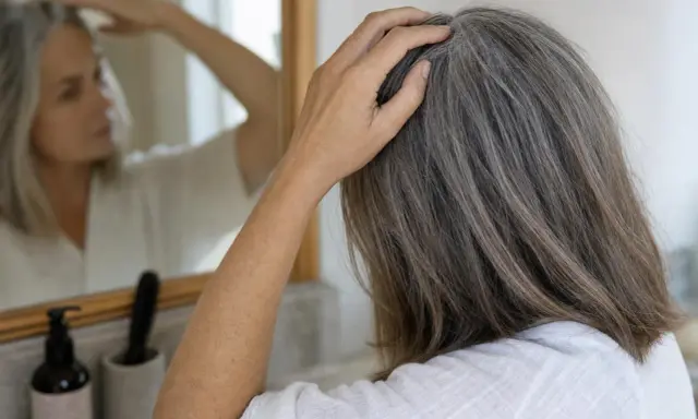 Donna con capelli grigi si tocca la testa, preoccupata che non pettinare i capelli li fa cadere.