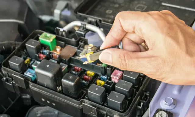 Wymiana bezpiecznika w Audi A3 8L pod maską. Dłoń trzyma wyjęty bezpiecznik, obok skrzynka z bezpiecznikami i przekaźnikami.