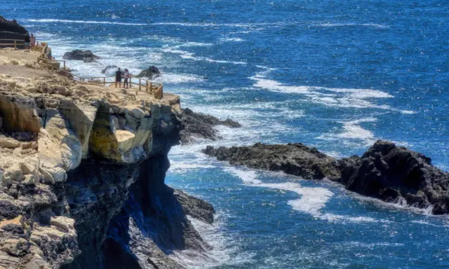 Acantilados rocosos y el mar azul cerca de las cuevas de Ajuy. Turistas observan el paisaje desde un mirador.