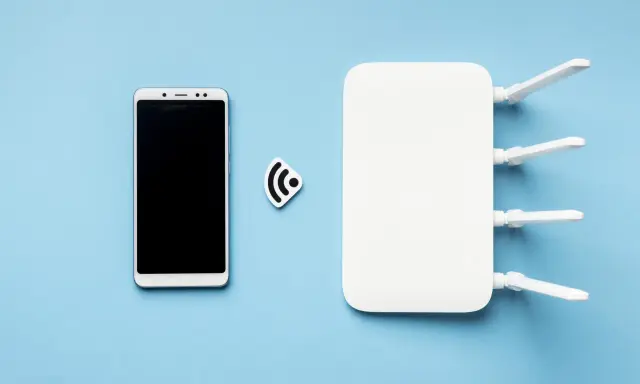 Biały router wifi z antenkami i smartfonem obok. Ikona sygnału wifi symbolizuje połączenie.