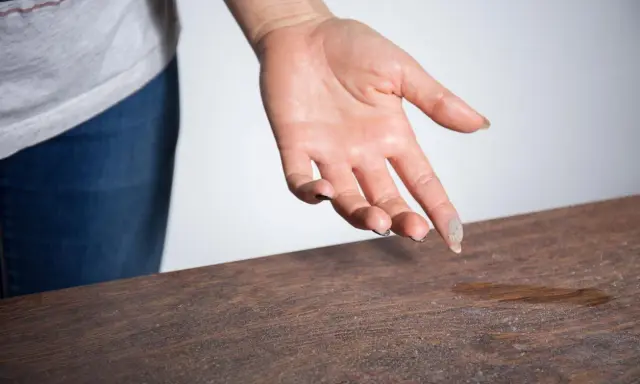 Mano con polvo en los dedos sobre una mesa de madera, mostrando porque sale tanta pelusa en casa.