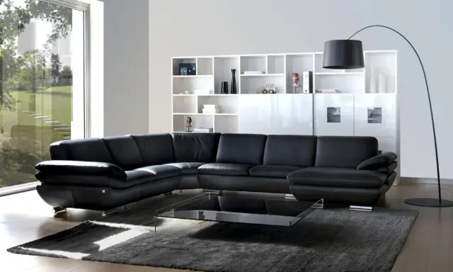 Sofá modular negro de cuero, con mesa de centro de cristal y estanterías blancas. Un diseño de gran dimensión.
