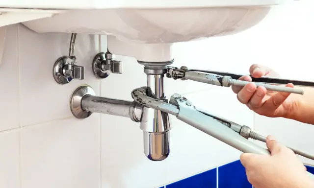 Mains de plombier resserrant un siphon qui fuit sous un lavabo blanc.