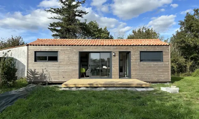 Une petite maison en bois avec une terrasse, idéale pour un plan maison 5m sur 10m. Le toit est couvert de tuiles rouges.