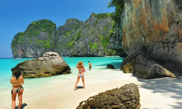 Två personer njuter av det turkosa vattnet och de dramatiska klipporna vid Maya Bay, Thailand.