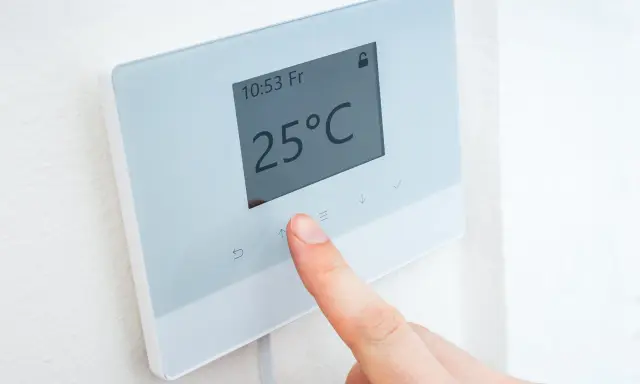 Dedo ajustando uno de los tipos de termostatos para calefacción, mostrando 25°C.