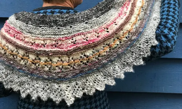 Un chal de lana tejido con hilos de colores, con un intrincado diseño de encaje y bordes festoneados. Los mantoncillos de crochet son una obra de arte.