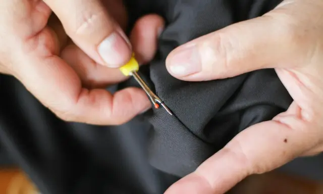 Hands use a seam ripper to open a pocket on black fabric. This is how suit pockets are sewn shut to maintain their shape during shipping.