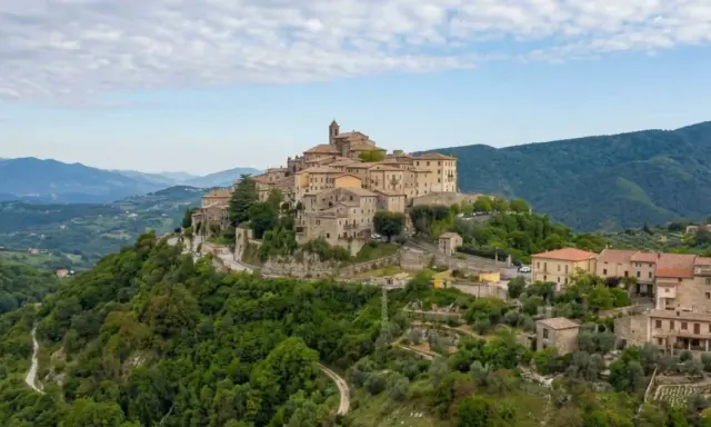 Borgo medievale su una collina verde, uno dei tanti **paesi da vedere vicino Roma**, con case in pietra e un campanile.