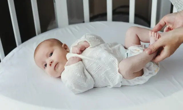 Noworodek w białej koszulce leży w łóżeczku, a ręce dotykają jego stóp.